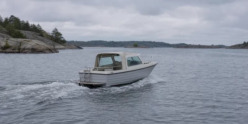 Liten vit motorbåt under gång i skärgården en grå mulen dag, med kölvatten efter aktern och kala klippor till vänster